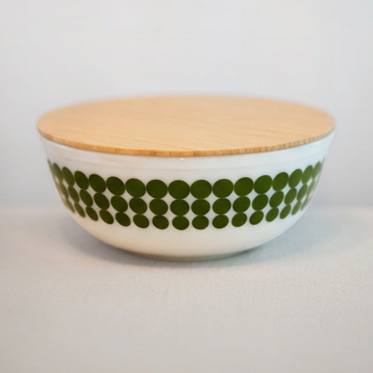 Ceramic bowl with green pattern and wooden lid on a light gray background