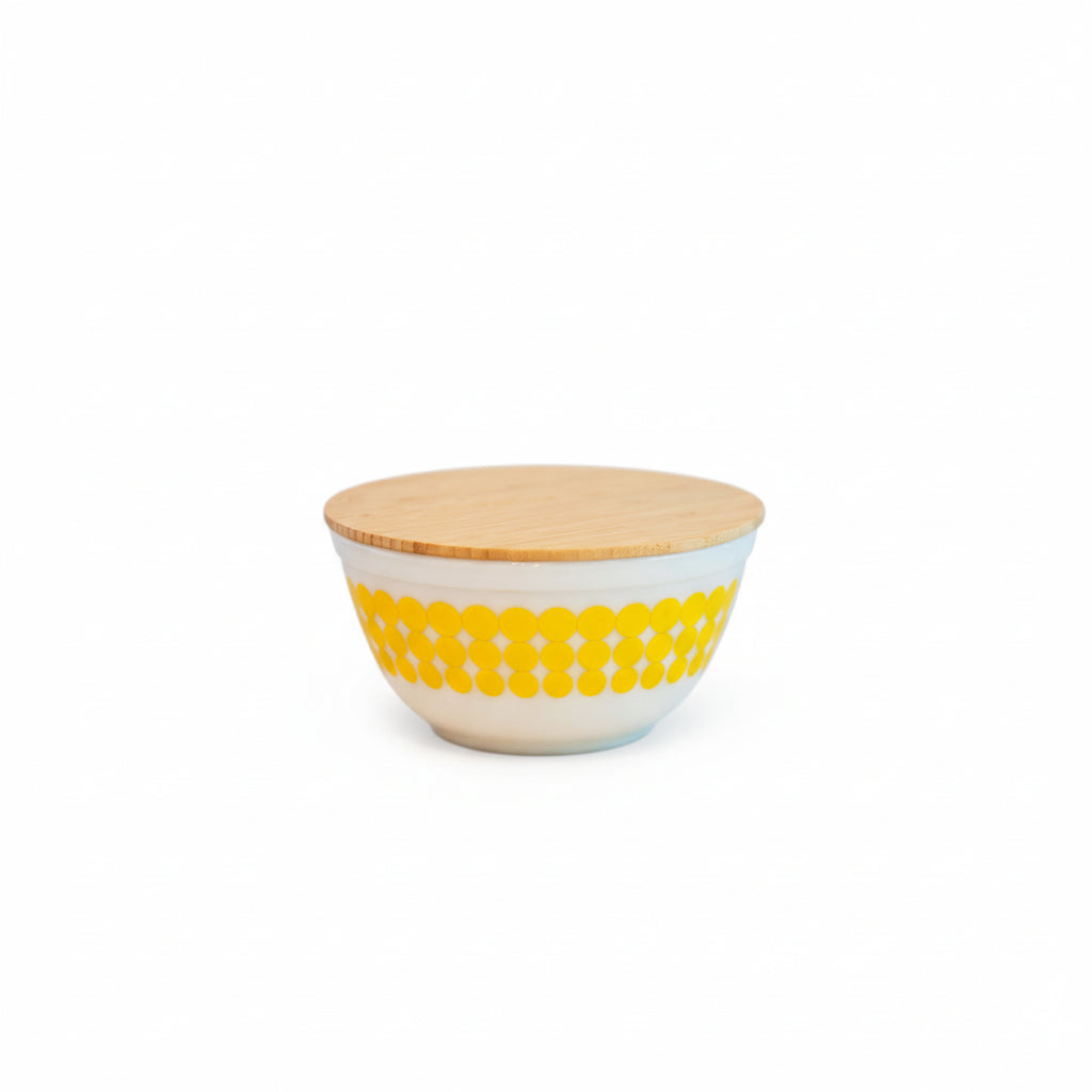 Ceramic bowl with yellow pattern and wooden lid on a white background